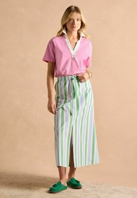 Ružová košeľa s krátkym rukávom a bielym golierom, skombinovaná s maxi sukňou pruhovanej v zelených a modrých odtieňoch a zelenými nazúvacími topánkami so detalom mašle.