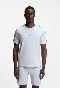 Vaaleansininen urheilupaita, jossa on lyhyet hihat, pyöreä kaulus, mustat olkasaumat ja keskellä rintaosassa logo "BOSS".