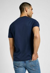 Granatowa bawełniana koszulka z krótkim rękawem, okrągłym dekoltem i gładką teksturą, pokazana z tyłu w połączeniu z niebieskimi dżinsami.