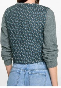 Zielony sweter z dzianiny z wzorzystym tyłem, przedstawiającym niebieskie motywy kwiatowe. Żebrowane rękawy i dół, średniej długości fason oraz miękka tekstura.