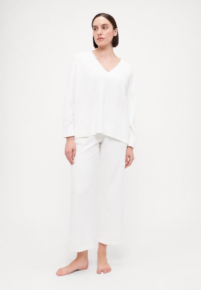 White knitted loungewear set featuring a V-neck, long sleeves, and wide-leg pants with cuffed hems, textured fabric, and a relaxed fit.