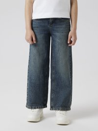 Wide-leg jeans in dark blue denim with a faded finish, featuring a straight fit, five-pocket design, and frayed hem, paired with white sneakers.