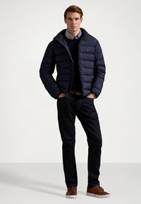 Tamsiai mėlyna pūkinė striukė su siuvinėtu raštu, užtrauktuku ir aukštu apykakliu, derinama su juodu džemperiu ir tamsiais džinsais. Ruda avalynė užbaigia įvaizdį.