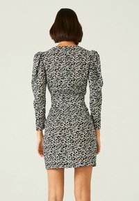 Zwart-witte luipaardprint jurk met lange pofmouwen, een getailleerde taille en een korte zoom. Glad stof met een lichte textuur.