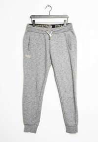 Szare dresowe spodnie z polaru z elastycznym pasem, białym sznurkiem, bocznymi kieszeniami i zakończeniami w ściągacze wiszące na czarnym wieszaku na białym tle.