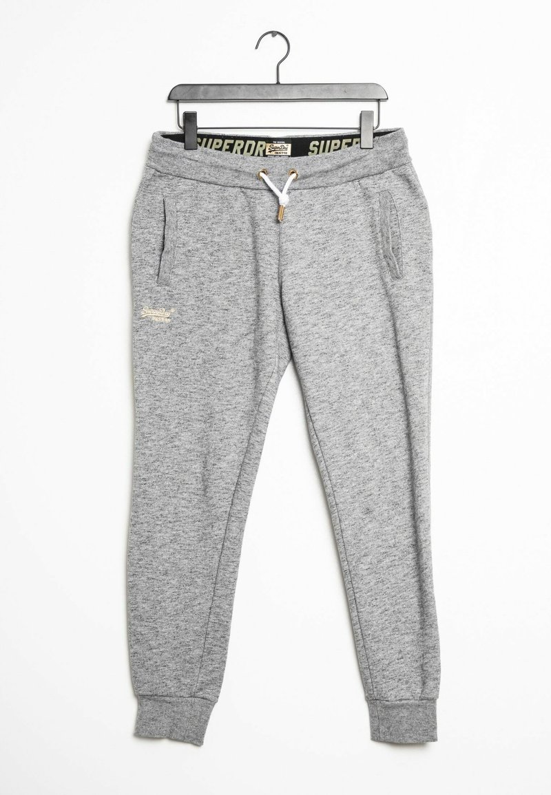 Szare dresowe spodnie z polaru z elastycznym pasem, białym sznurkiem, bocznymi kieszeniami i zakończeniami w ściągacze wiszące na czarnym wieszaku na białym tle.