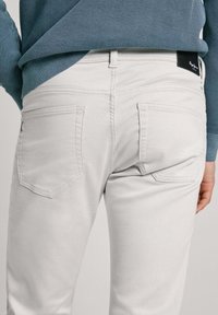 Bela denim hlače z dvema zadnjima žepoma in subtilnimi šivi. Oblečene z teksturirano modro jopico, kar razkriva sproščen stilski izgled.