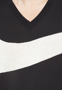 Gros plan sur un pull noir en V avec une large bande diagonale blanche à travers la poitrine.