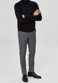 Czarny sweter z golfem, szare teksturowane spodnie i czarne eleganckie buty. Spodnie mają dopasowany krój i subtelny wzór w kratkę.