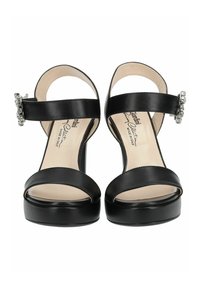 Sandales à talons hauts en cuir noir avec un bout ouvert, une bride à la cheville et une quincaillerie argentée embellie sur le côté. Texture lisse, design minimal.