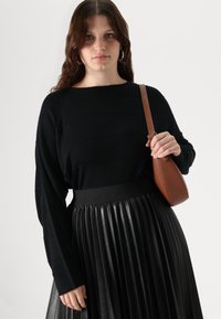 Svart langermet genser med horisontal ribbet tekstur, kombinert med et høyhåndt pleated svart skjørt og en brun crossover-veske.