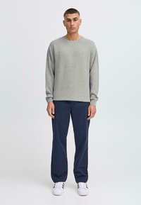 Grau gestrickter Pullover mit Rundhalsausschnitt und langen Ärmeln, kombiniert mit dunkelblauen Hosen und weißen Sneakers. Einfaches, entspanntes Design.