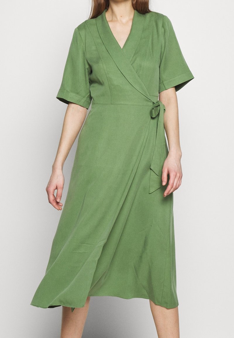 Vestito avvolgente verde in tessuto morbido, con maniche corte, scollatura a V e una cintura annodata in vita, dotato di una gonna A-line fluida.