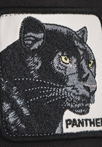 Sort broderet mærke med et pantherhoved med gule øjne, omridset i grå, sat mod en hvid baggrund med ordet "PANTHER" nedenfor.