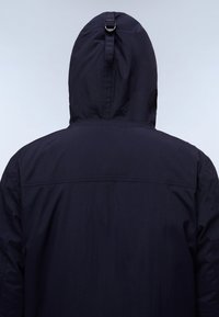 Chaqueta con capucha de color marino vista desde la parte de atrás, con una textura suave, correa ajustable para la capucha y un diseño sencillo sin logotipos visibles.