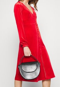 Röd sammetklänning med långa ärmar och djup V-ringning, med en knapp-down framtill. Svart handväska med krokodilpr Präglat mönster och en böjd design.