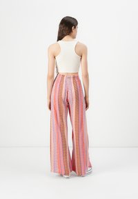Pantalons à jambes larges en rose et orange avec des motifs géométriques. Associés à un haut en débardeur crème ajusté. Style décontracté, tissu léger.