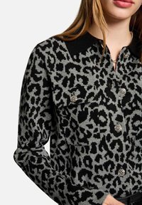 Camicia a maniche lunghe con stampa leopardata in tessuto a maglia grigio e nero. Presenta un colletto nero e bottoni decorativi argento sulle tasche del petto.