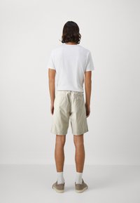 T-shirt blanc pour homme, vue de dos, associé à un short beige clair. Le short a une coupe décontractée, une taille élastique et est fabriqué en tissu léger.