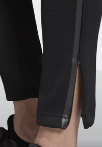 Svarta träningsbyxor med sidodragkedja vid ankeln, slät struktur och slim fit-design med en kontrasterande mörk rand.