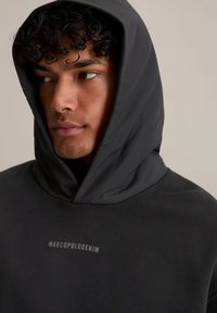 Ciemnoszara bluza z kapturem wykonana z miękkiego materiału, z wyraźnym logo "MARCOPOLODENIM" w jasnoszarym kolorze z przodu.