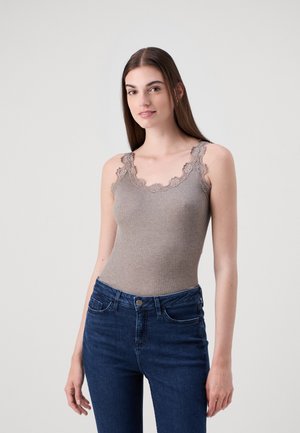 Rybkovaný top v taupe s krajkovým lemem na výstřihu, kombinovaný s modrými dobře padnoucími džíny. Modelka pózuje ve stoje, s uvolněnýma rukama podél těla.