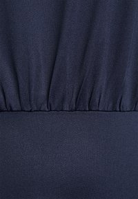 Tecido azul marinho com um acabamento texturizado, apresentando elástico franzido na cintura e áreas lisas para um design estruturado.