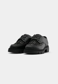 Chaussures en cuir noir avec un panneau en tissu texturé présentant un motif gris et blanc. Semelle en caoutchouc épaisse avec un design à lacets et un bout arrondi.