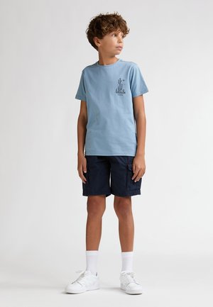 T-shirt en coton bleu clair avec un motif de cactus sur la poitrine gauche, associé à un short cargo bleu marine et des baskets blanches, avec un col ras du cou côtelé.