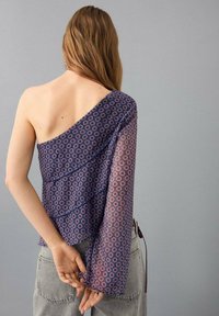 Jednobarevný top s jedním ramínkem v námořnické modři s geometrickým vzorem, průhlednými dlouhými rukávy a volánkovým designem. Má volný střih a zavazování na boku.