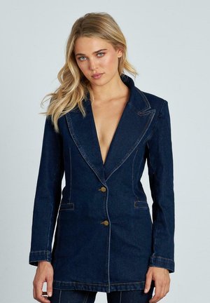 Blazer de denim de color azul oscuro con un escote en V profundo, solapas con muesca, dos bolsillos frontales y acentos de botones dorados. Detalle de costura visible en todo el diseño.