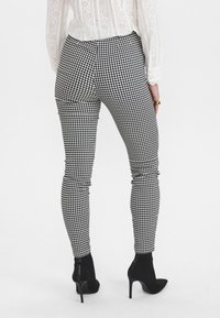 Černobílé kárované zúžené kalhoty s hladkou texturou, s bočním nařasením, doplněné černými vysokými kozačkami.