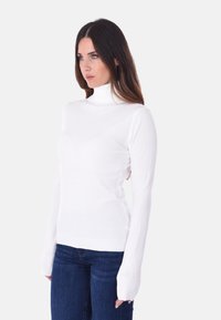 Maglione a collo alto bianco con maniche lunghe e aderenti, polsini e orlo a coste, realizzato in materiale liscio, abbinato a jeans blu.