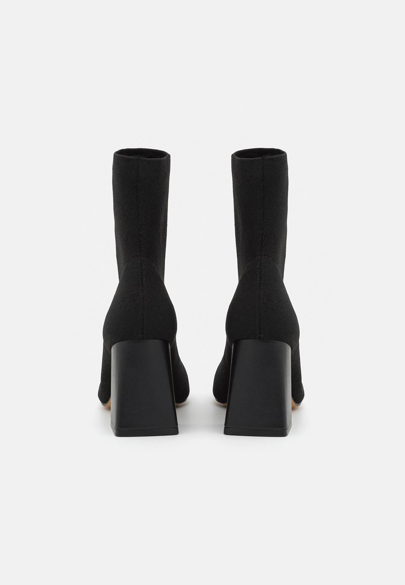 Schwarze Stiefeletten aus Stoff mit glatter Textur, ausgestattet mit einem quadratischen Absatz und einer figurbetonten Silhouette. Die Rückansicht zeigt minimale Details.