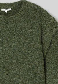 Pull en laine tricoté vert avec un col rond, fabriqué en laine texturée, avec des manches courtes et un motif chiné subtil. Étiquette de taille visible.