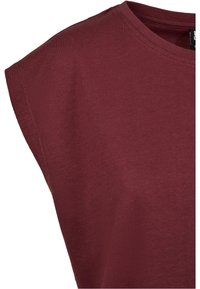 Gros plan sur une chemise sans manches en coton bordeaux montrant l'épaule et l'encolure ronde avec des détails de coutures visibles.