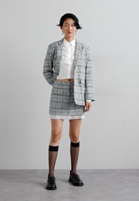 Gray plaid blazer over a white cropped shirt, paired with a matching skirt. Features black knee-high socks and lace-up black shoes.