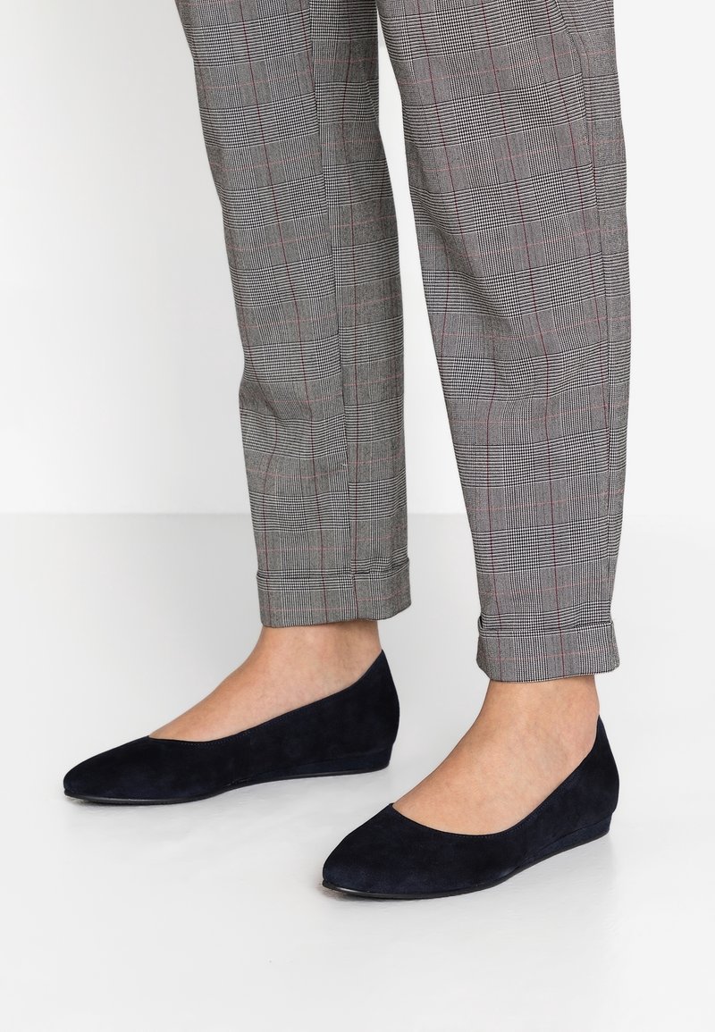 Ballerines en daim bleu marine à bout fermé et talon légèrement compensé, assorties à un pantalon à carreaux gris avec des lignes rouges et noires.