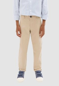 Pantalons en coton beige avec une coupe droite, dotés d'une fermeture par bouton, de poches avant, associés à des baskets navy. Chemise rayée bleu et blanc au-dessus.