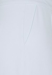 Close-up of light grey fabric with a vertical seam and slight curved stitch detailing near the top edge.