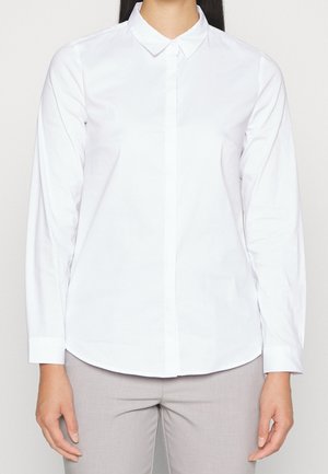 White long-sleeve shirt with a pointed collar, buttoned front, and a smooth, crisp texture. Features a curved hemline.