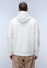 Sudadera blanca con capucha ajustable, textura suave, mangas largas, puños y dobladillo de canalé, combinada con pantalones ligeros beige.