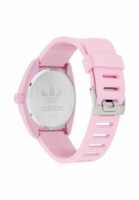 Montre en silicone rose avec un dos en acier inoxydable argenté, dotée d'un boîtier rond, d'un bracelet texturé et d'une boucle métallique réglable.