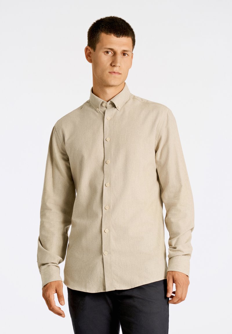 Camisa beige claro de botones, hecha de tela texturizada, con cuello y mangas largas. Detalles de costura sutiles visibles.