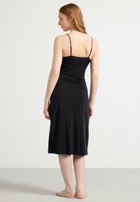 Schwarzes ärmelloses Kleid aus glattem Stoff, knielang, mit dünnen verstellbaren Trägern und einer gerafften Nahtdetails auf der Rückseite.