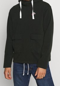 Dark green hooded sweatshirt with a drawstring, two front pockets, and white accents. Features a small logo on the chest. Cotton material.