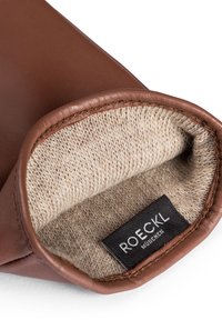 Interno di un guanto di pelle marrone con morbido rivestimento in maglia beige e un'etichetta nera del marchio. Il polsino è liscio e stondato, mostrando cuciture di qualità.