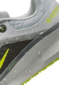Gros plan d'une chaussure Nike grise et noire avec des accents jaunes, des gouttes d'eau sur la surface, et la marque Gore-Tex Invisible Fit.