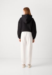 Felpa nera cropped con cappuccio, abbinata a pantaloni joggers bianchi con vita elastica e sneakers beige con zeppa. Tessuto liscio, vestibilità comoda.