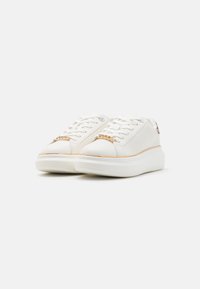 Baskets blanches avec une tige en cuir lisse, des accents dorés sur le bout et une épaisse semelle en caoutchouc blanc avec un motif de traction texturé.